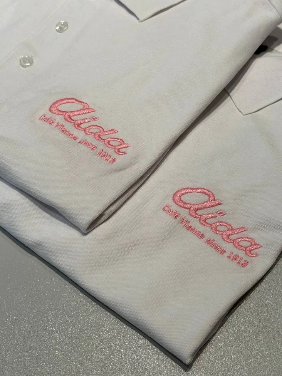 Aida Café Vienna Logo-Stickerei auf weißem Poloshirt