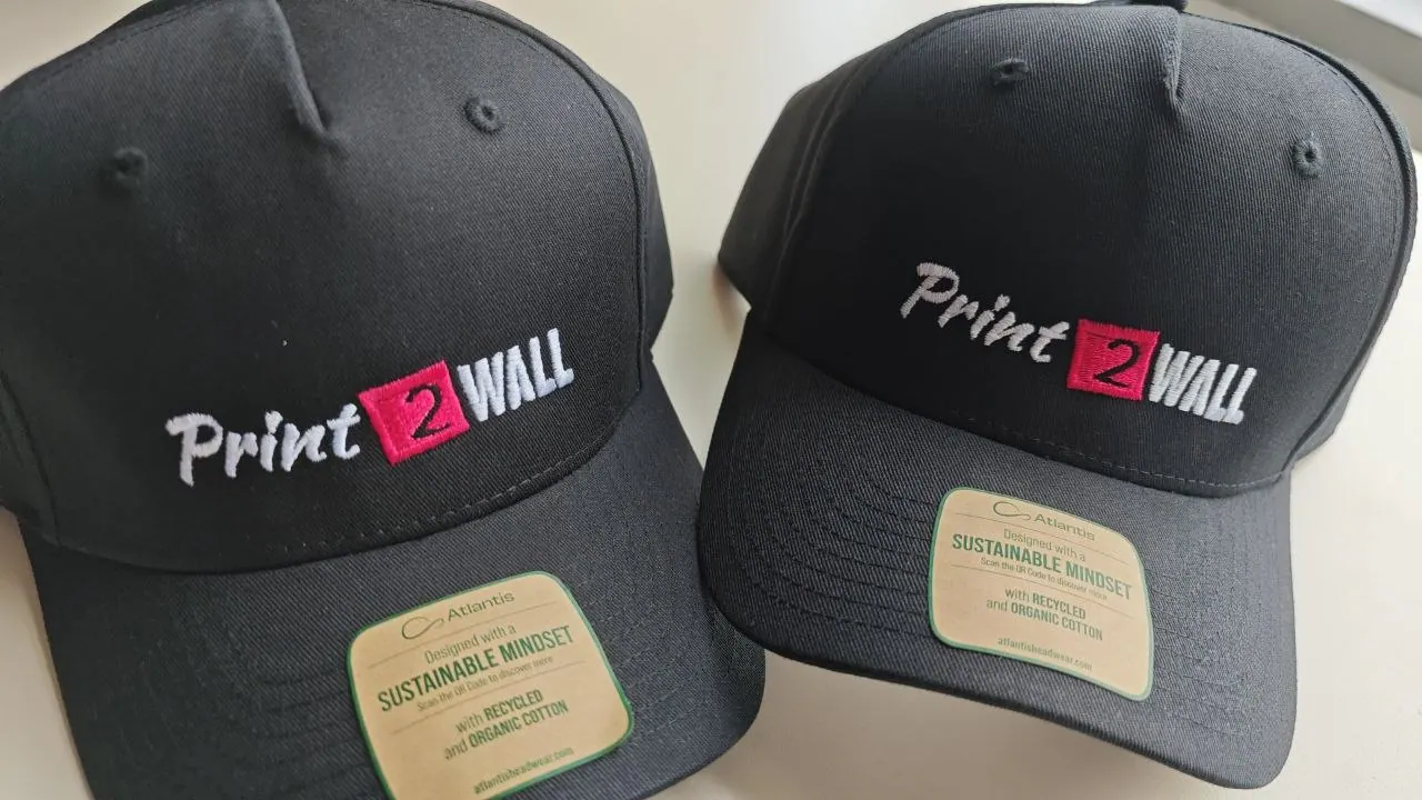 Zwei schwarze Basecaps mit gestickter Print2Wall Logostickerei in weiß und pink – nachhaltige Atlantis Kappen aus recycelter Bio-Baumwolle