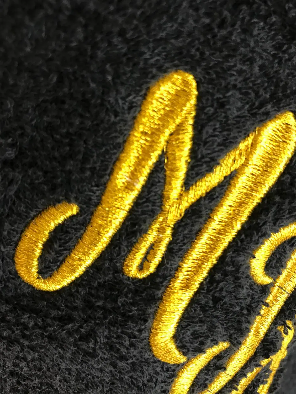 Goldene Buchstaben-Stickerei auf schwarzem Frottee – edle Schreibschrift Detail