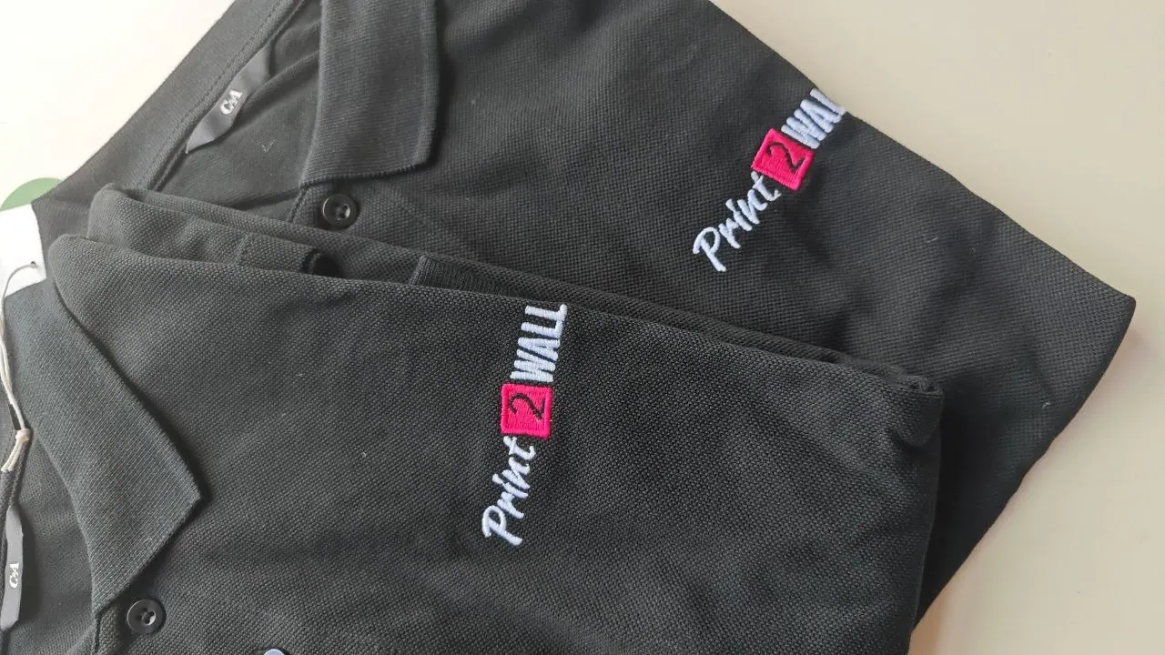 Zwei schwarze Poloshirts mit gestickter Print2Wall Logostickerei in weiß und pink – Team-Bekleidung
