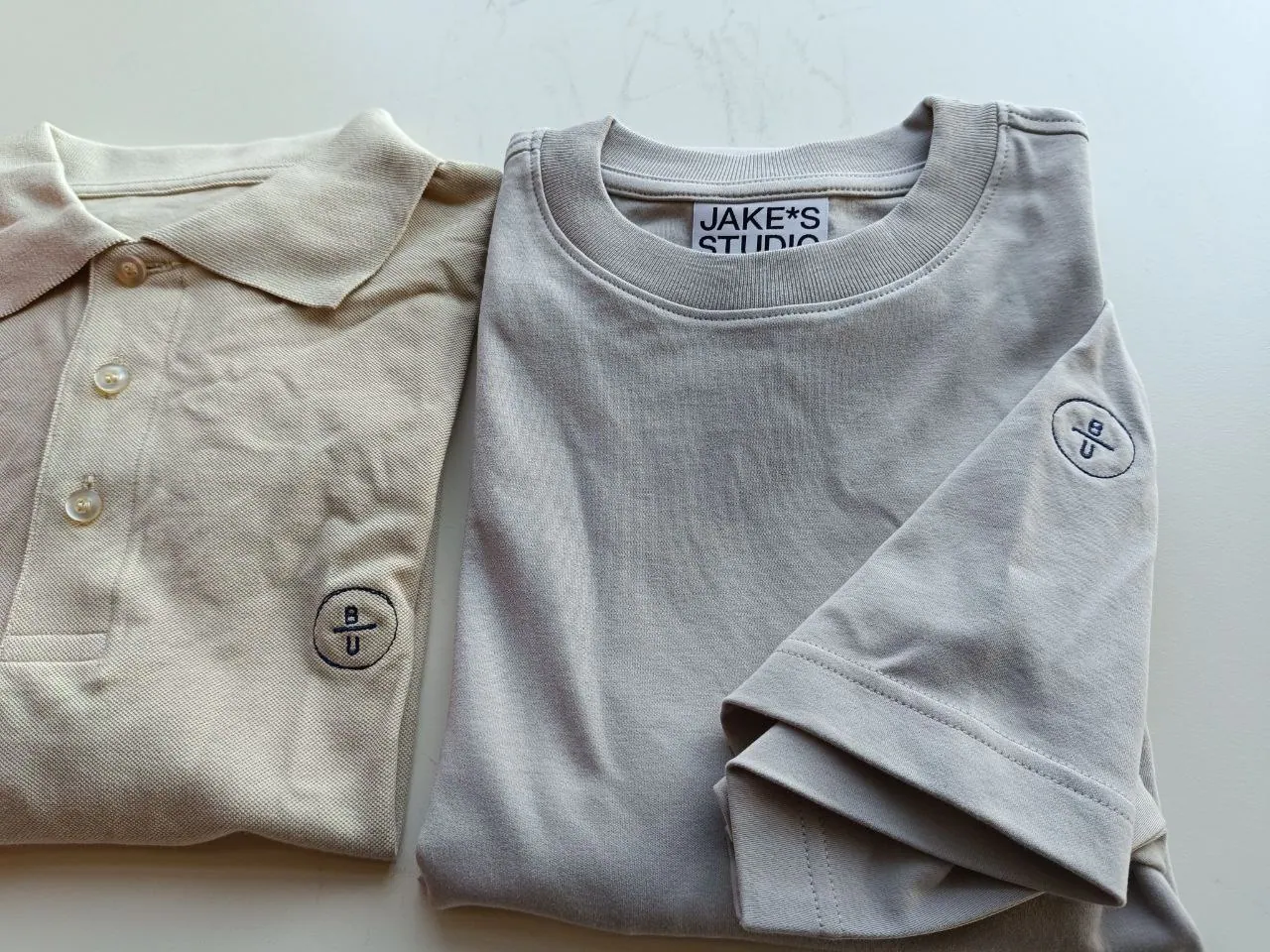 Beiges Polo und graues T-Shirt mit kleiner BU Logo-Stickerei am Ärmel – Gastronomie-Bekleidung