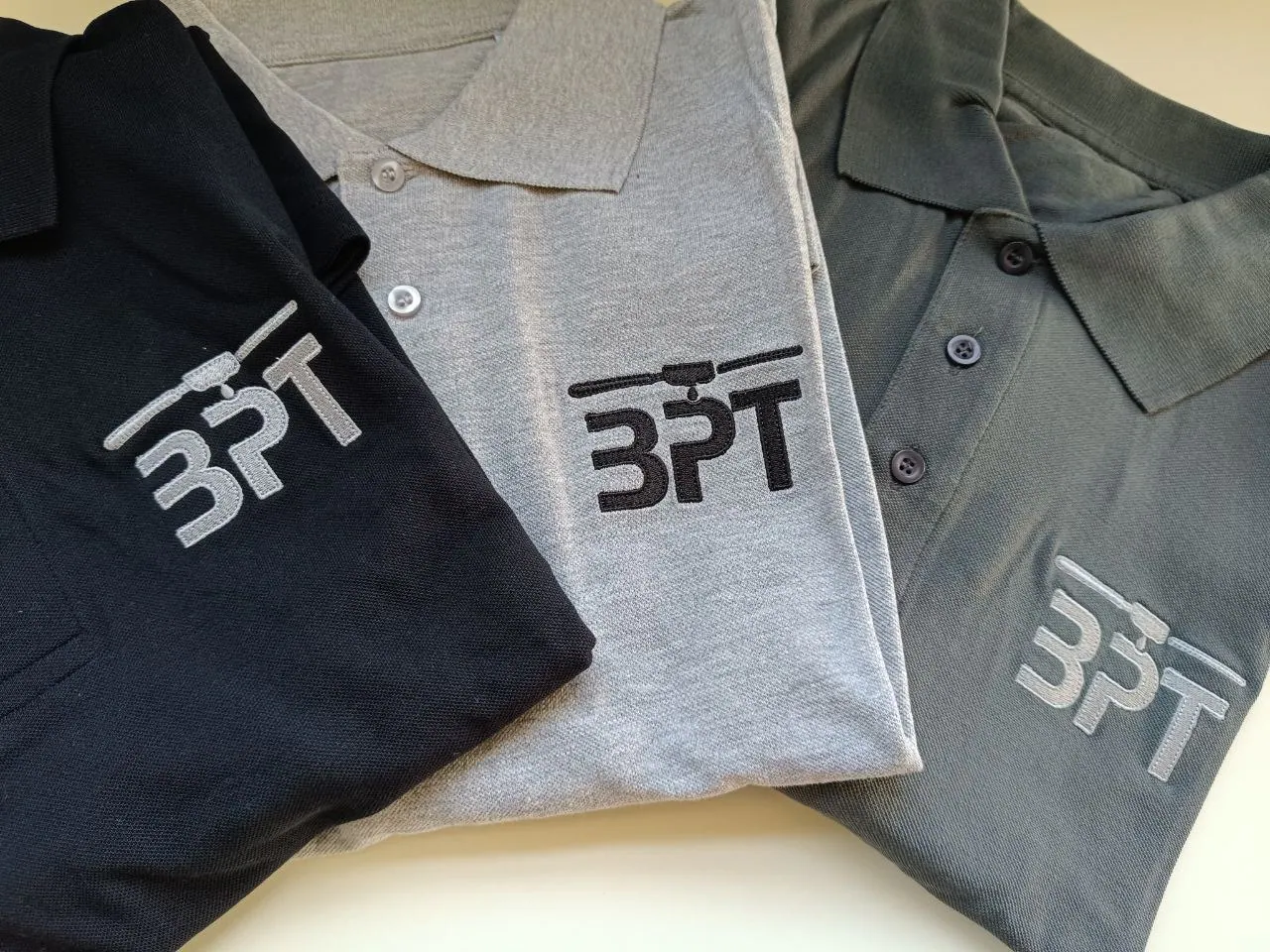 Drei Poloshirts in schwarz, grau und oliv mit gesticktem BPT Firmenlogo – Berufsbekleidung